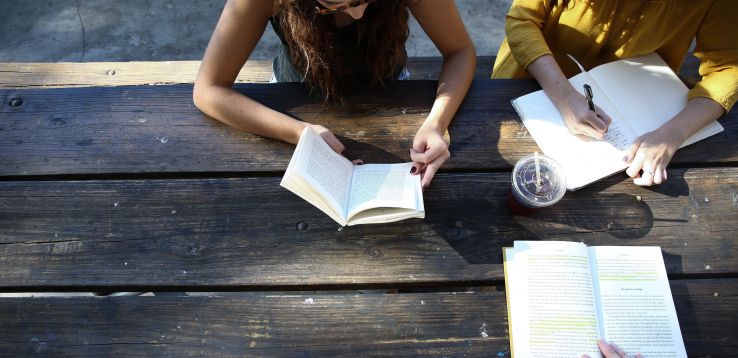 three women at a picnic table reading and writing