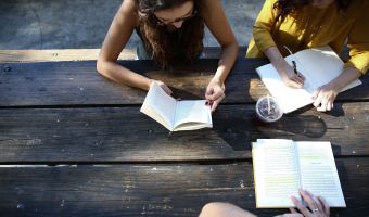 three women at a picnic table reading and writing